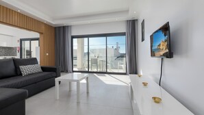 Een moderne woonkamer met een zwarte bank, een witte salontafel en een aan de muur bevestigde televisie.