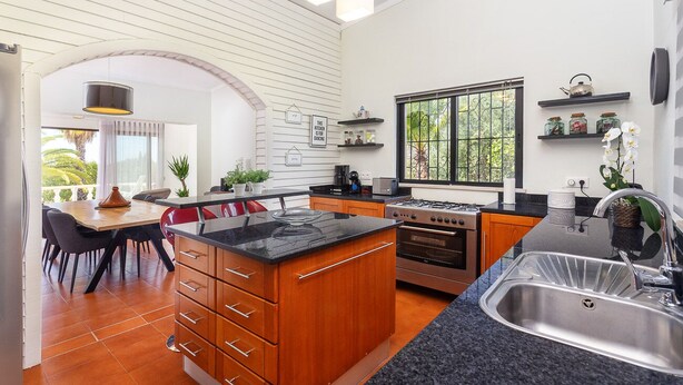 A modern kitchen with a central island, wooden cabinets, and a black countertop. There is a window with a view of greenery, a sink, and a stove. - Luxury 3-Bedroom Countryside Villa with Pool, Quelfes (Quelfes)