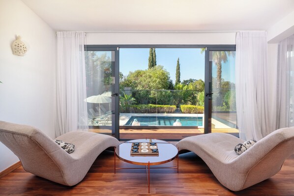 A room with two armchairs, a small table, and a glass door leading to a pool.