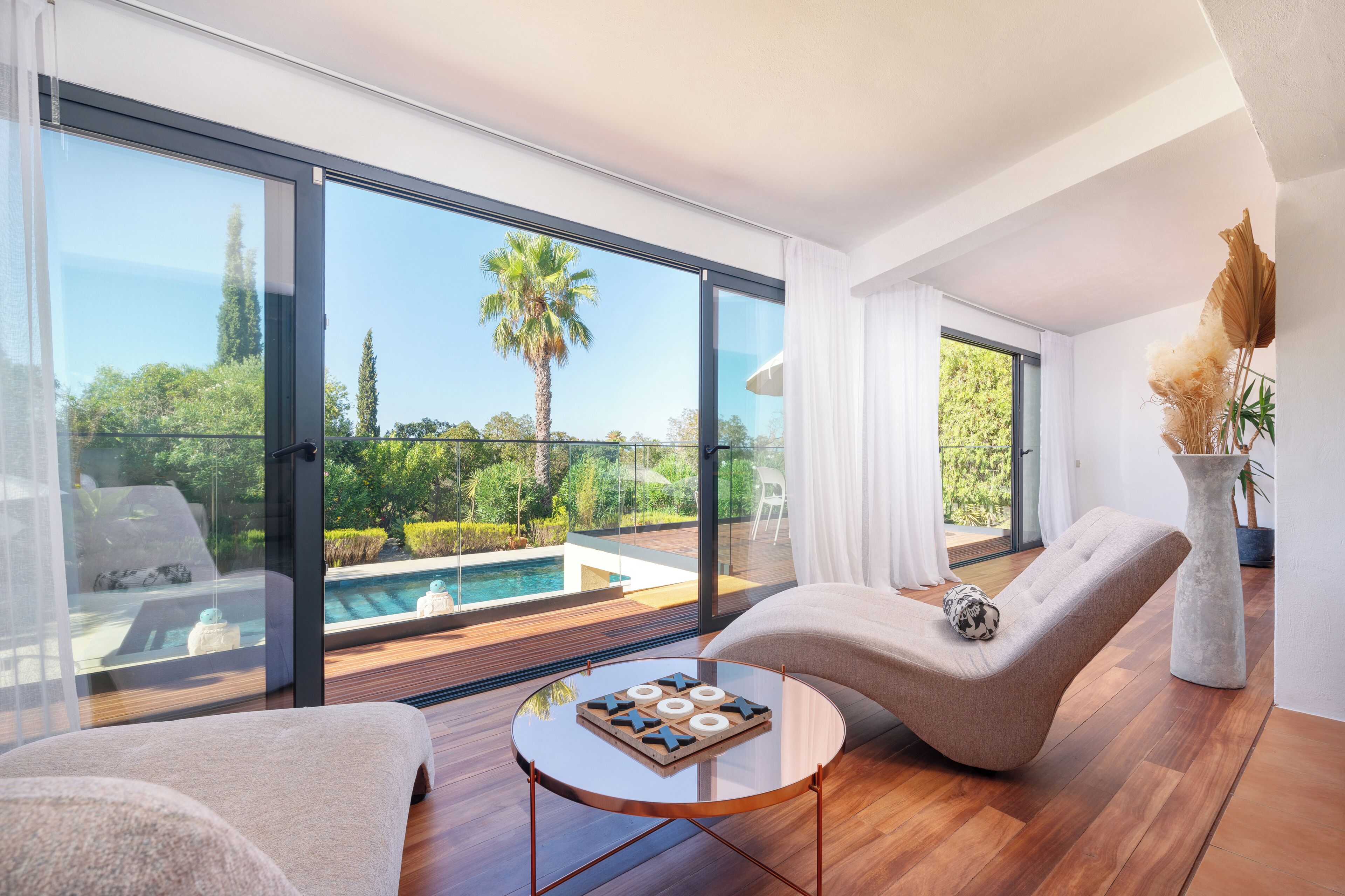Una sala de estar moderna con vista a la piscina, una mesa redonda para café y un área de descanso confortable.