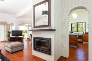 A modern living room with a fireplace, a television, and a kitchen visible through an archway. - Luxury 3-Bedroom Countryside Villa with Pool, Quelfes (Quelfes)