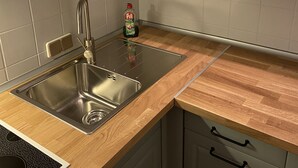Una cocina con armarios blancos, un lavamanos de acero inoxidable, una encimera de madera y una botella de detergente.