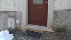 A brown door with a frosted glass panel, a small porch with a wooden railing, and a wall-mounted light fixture. - Little Paradise in the center of Rivisondoli (Rivisondoli)