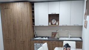 A compact kitchen with wooden cabinets, a white countertop, and a dining table with a patterned tablecloth. - Little Paradise in the center of Rivisondoli (Rivisondoli)