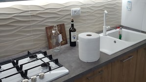 A kitchen with a gas stove, a microwave, a sink, and a countertop with a bottle of wine and a roll of paper towels. - Little Paradise in the center of Rivisondoli (Rivisondoli)
