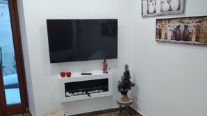 A living room with a flat-screen TV mounted on a white wall, a small wooden stool, and a grey sofa. - Little Paradise in the center of Rivisondoli (Rivisondoli)