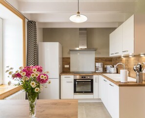 A modern kitchen with white cabinets, a wooden countertop, a built-in oven, and a hanging light fixture.