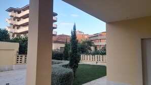 Un balcon donnant sur une cour, avec un grand arbre et des immeubles d’habitation en arrière-plan.