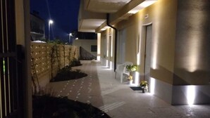 Un couloir avec un sol carrelé, une chaise blanche et une petite table sur laquelle est posée une plante.