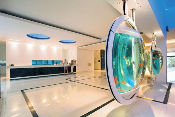 Eine moderne Hotelhalle mit einer Rezeption, einem Glasaquarium und einem sauberen, gefliesten Boden.