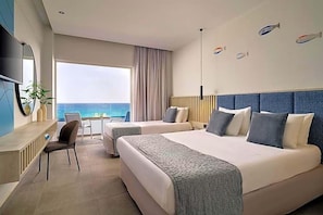 Una camera d'albergo con due letti, una scrivania, una sedia, una televisione e vista sul mare.