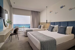 Habitación de hotel con dos camas, un escritorio, una silla y un ventanal con vistas al mar.
