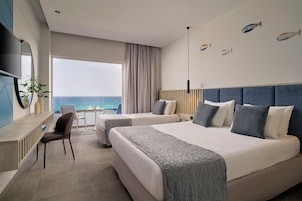 Habitación de hotel con dos camas, un escritorio, una silla y un ventanal con vistas al mar.