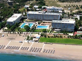 Vista aérea de un resort con varias construcciones, una piscina grande y una zona de playa con tumbonas.