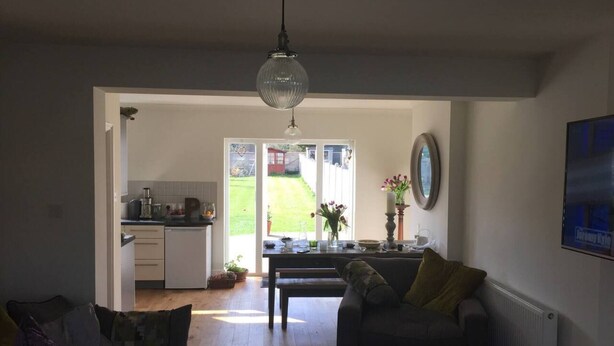 Un salón amplio con un ventanal, un comedor con mesa y sillas, y una cocina al fondo.