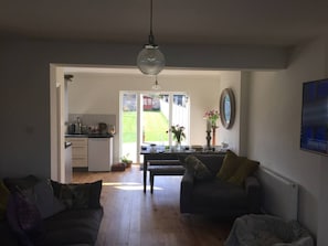 Un vaste salon avec une grande fenêtre, un coin repas avec une table et des chaises, et une cuisine à l’arrière-plan.