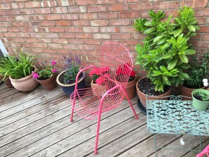 A wooden deck with potted plants and a pink metal chair. - Beautiful 3-bed House in Ramsgate (Ramsgate)