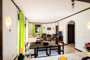 Un comedor con una mesa, sillas y un televisor. En el fondo, un sofá y una chimenea.