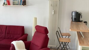 Un salon avec un canapé rouge, une petite table en bois, un radiateur et une bibliothèque remplie de livres.