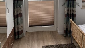 Une pièce avec une grande fenêtre, un plancher en bois, un lit et une armoire.