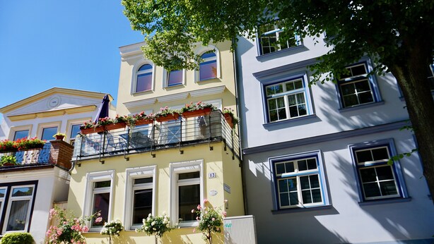 Une rangée de bâtiments de style européen, dotés de balcons et de jardinières fleuries, sous un ciel d’un bleu éclatant.