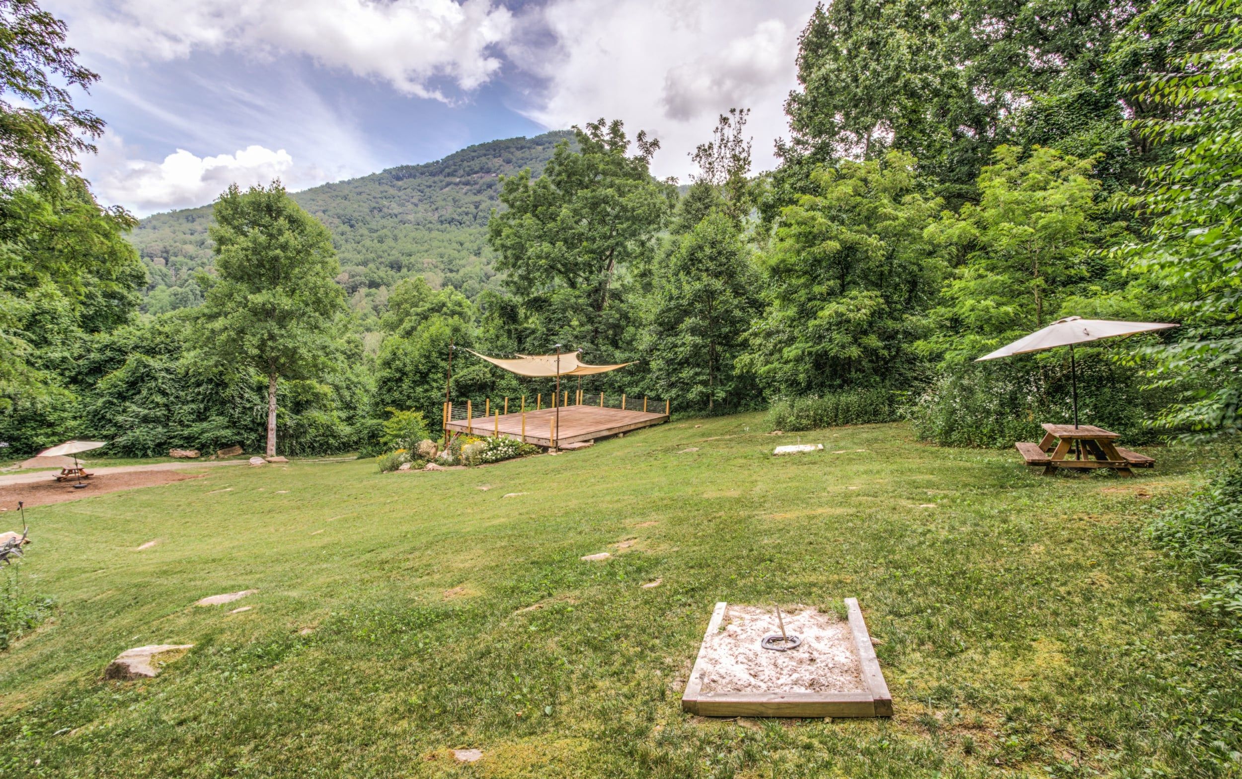 A grassy outdoor area with a wooden deck, picnic table, and umbrella.