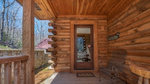 A wooden cabin with a porch, a bench, and a door leading to a covered area with a table and chairs. - Nature's Den | Pet-Friendly, Mountaintop Cabin in Columbus (Columbus)