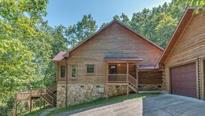A log cabin with a stone foundation, a porch, and a garage. - Nature's Den | Pet-Friendly, Mountaintop Cabin in Columbus (Columbus)