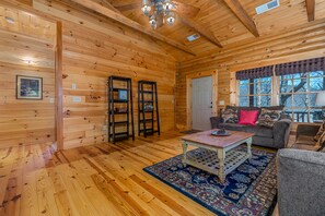 A wooden cabin interior with a sofa, coffee table, and a patterned rug.