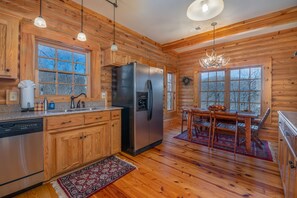 A wooden cabin kitchen with a stainless steel refrigerator, wooden cabinets, a dining table with chairs, and a chandelier.