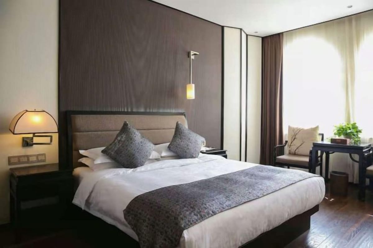 A hotel room with a large bed, bedside tables, a desk, and a window with curtains.
