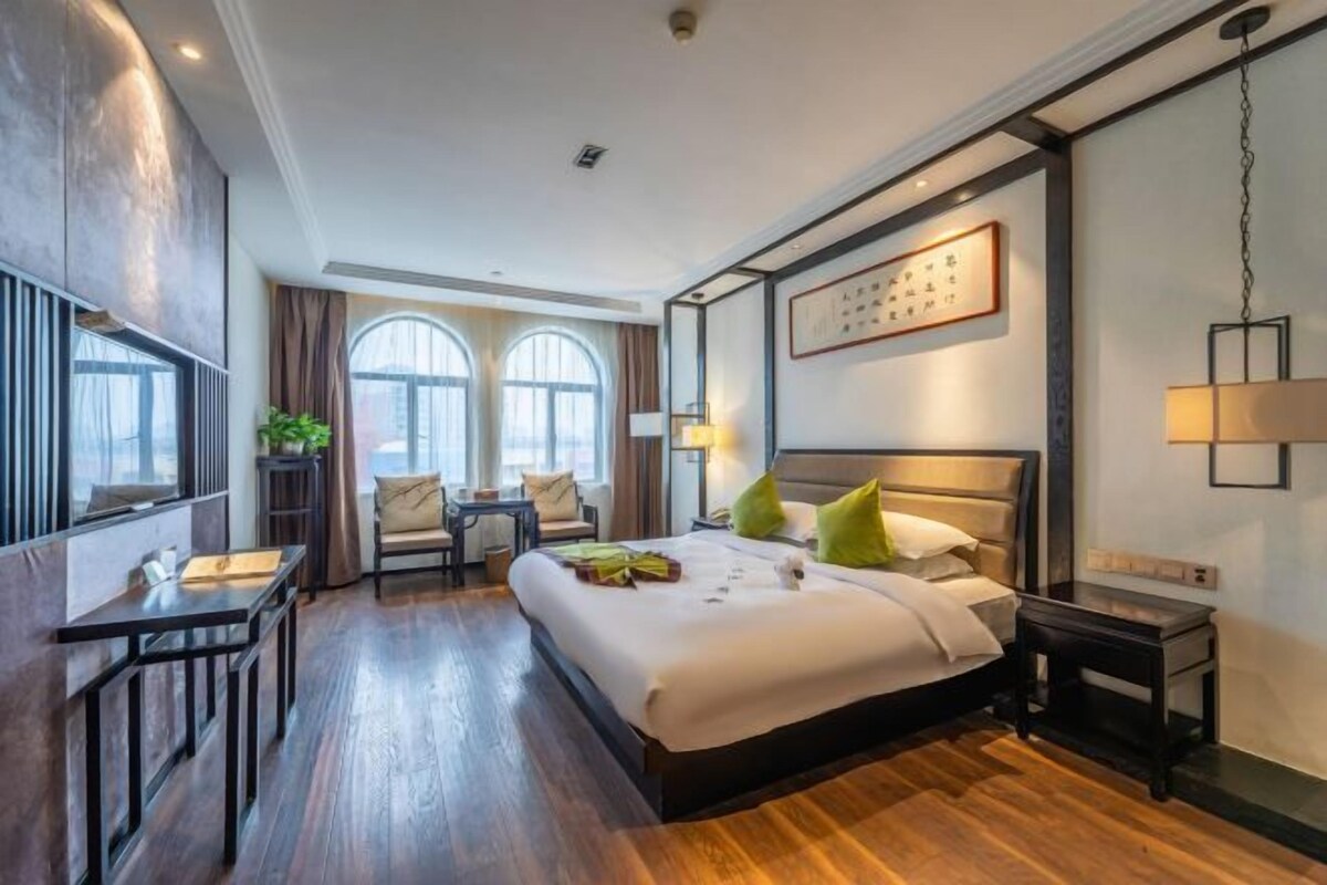 A hotel room with a large bed, a desk, a chair, and two windows.