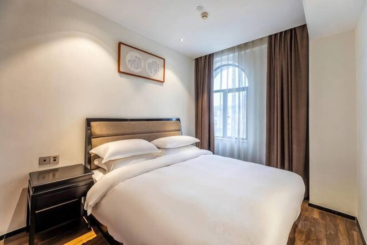 Hotellihuone, jossa on suuri sänky, yöpöytä, seinälle ripustettu taideteos ja ikkuna, jossa on verhot.
