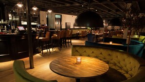 Eine moderne Bar mit einer Holztheke, mehreren Barhocker und einer Sitzecke mit rundem Tisch und gepolstertem Sitz.