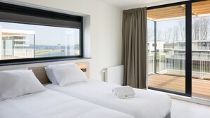 A modern hotel room with two beds, a large window, and a view of a building and water. - Luxury Villa With Jetty, at the Veerse Meer (Arnemuiden)