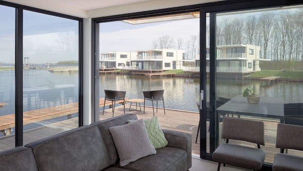 A modern living room with a large window overlooking a water body and a dock. - Luxury Villa With Jetty, at the Veerse Meer (Arnemuiden)