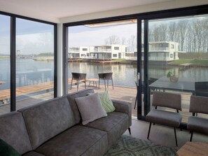 A modern living room with a large window overlooking a water body and a dock. - Luxury Villa With Jetty, at the Veerse Meer (Arnemuiden)