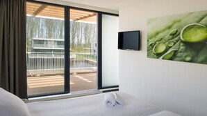 A hotel room with a bed, a TV mounted on the wall, and a large window with a view of a building and trees. - Luxury Villa With Jetty, at the Veerse Meer (Arnemuiden)