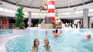 An indoor swimming pool with a central fountain, surrounded by a tiled deck and potted plants. - Modern Chalet With Garden, in Green Kempen (Mol)