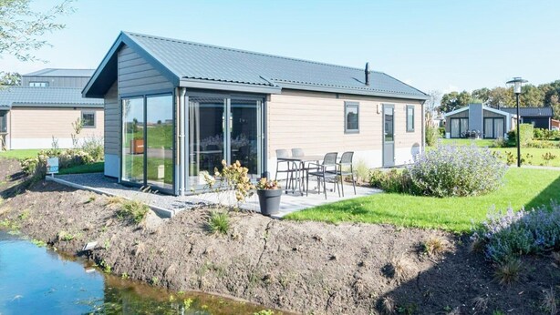A modern house with a glass conservatory, a patio with chairs, and a small garden.