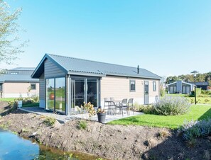 A modern house with a glass conservatory, a patio with chairs, and a small garden. - Comfortable Chalet Located in the Polder, Near Alkmaar (West-Graftdijk)