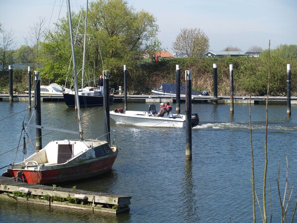 Un port de plaisance avec des bateaux amarrés, un voilier au premier plan et un bateau à moteur avec deux personnes à l’arrière-plan.