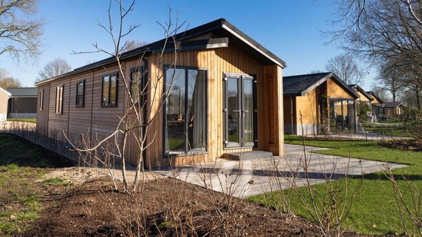 Una cabaña moderna de madera con amplias puertas de cristal, un pequeño porche y un césped cuidado.