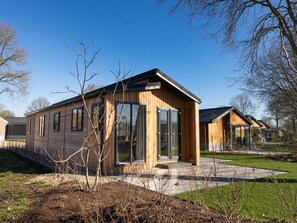 Une cabane moderne en bois, dotée de grandes portes vitrées, d’un petit porche et d’une pelouse bien entretenue.
