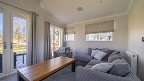 Una sala de estar moderna con un sofá, una mesa de centro de madera y vistas al exterior a través de amplios ventanales.