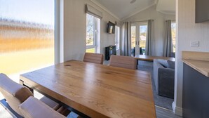 Un comedor amplio con una larga mesa de madera y sillas, un televisor montado en la pared y grandes ventanales que aportan luz natural.