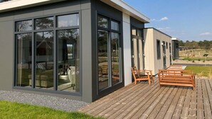 A modern house with large glass windows, a wooden deck, and a grassy yard. - Chalet With Dishwasher in the Green Kempen (Mol)