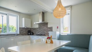 A modern kitchen with white cabinets, a stone backsplash, and a dining area with a white table and chairs. - Modern, Spacious, Detached Holiday Home, Near Alkmaar (West-Graftdijk)