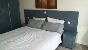 A neatly made bed with white and grey linens, a grey headboard, and a small bedside table with a drawer. - Modern Chalet With Combi-microwave (Brunssum)