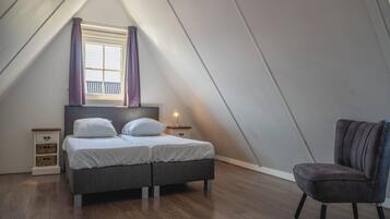 A bedroom with a bed, a chair, a nightstand, and a window with curtains.